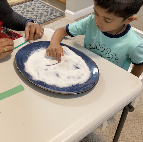 A boy putting his finger in a plate of white sand for special needs learning