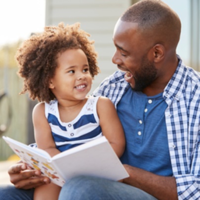 A girl child sitting on a man’s lap and they are both smiling